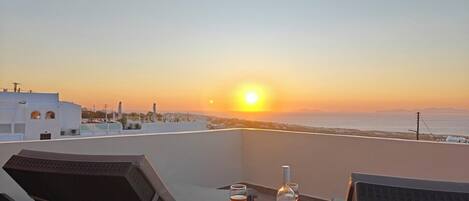 A sunset view from a balcony with a table set for two, including a bottle and glasses.