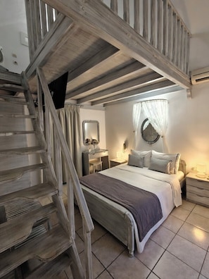 Un dormitorio con escalera de madera, una cama con almohadas, una mesita de noche y un espejo colgado en la pared.