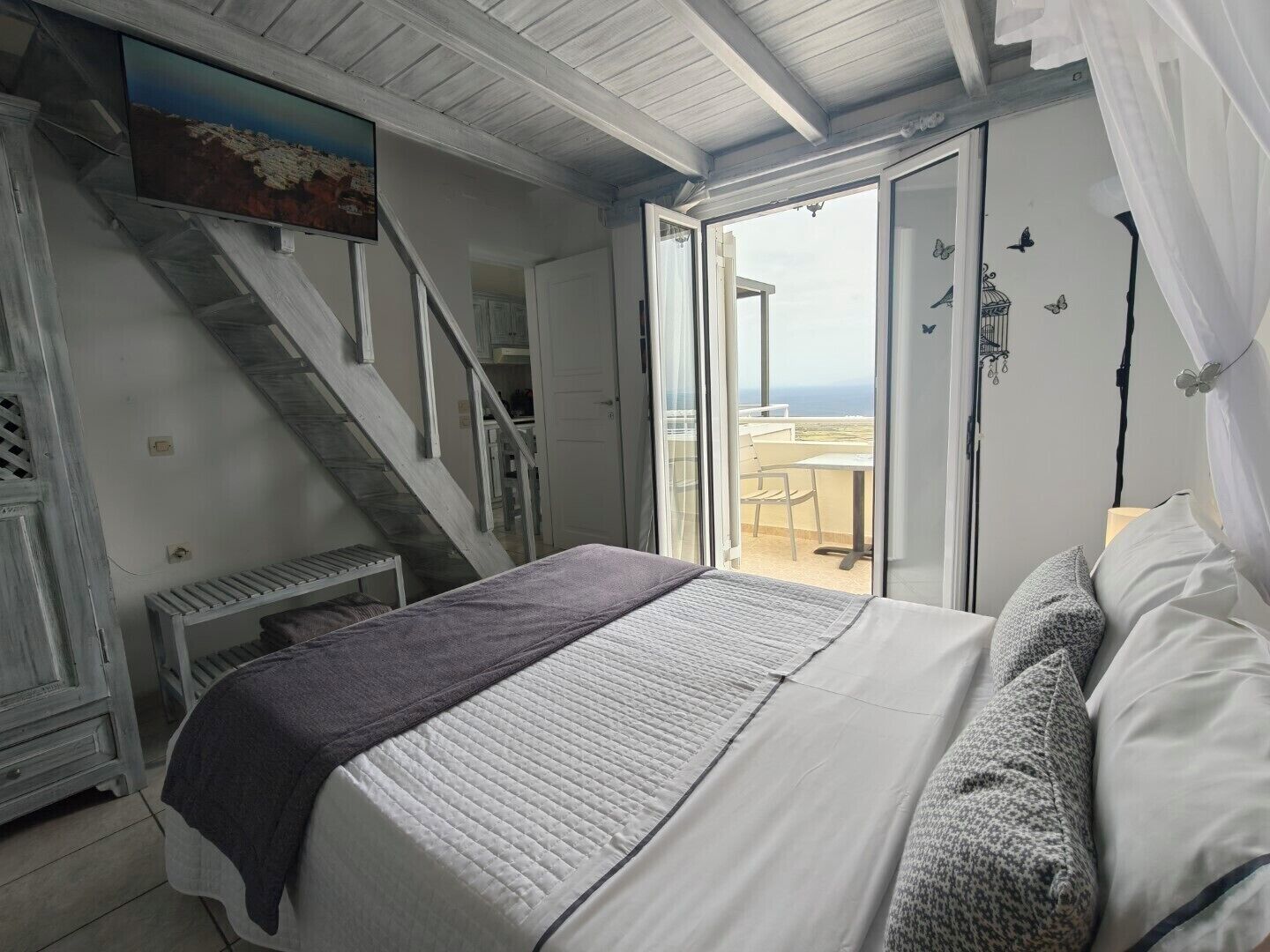 A bedroom with a bed, a staircase, a balcony with a view, and a painting on the wall.