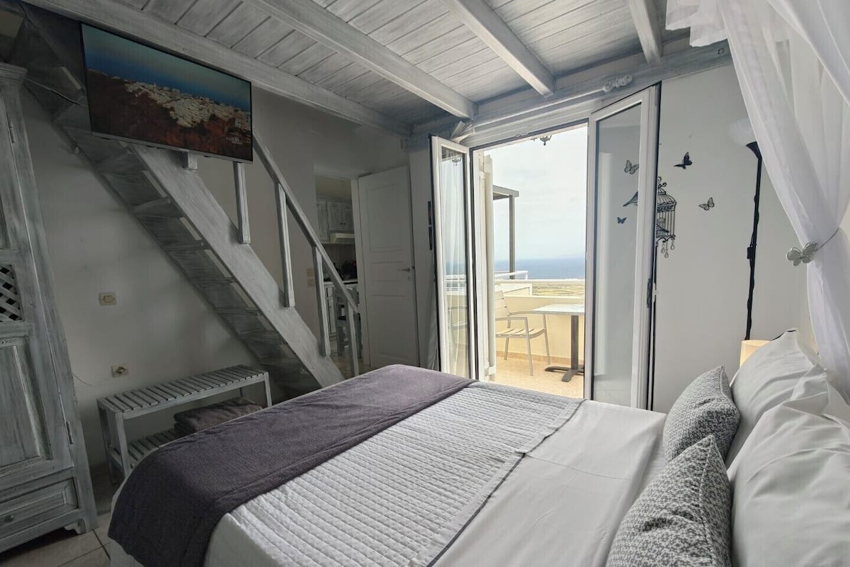 Un dormitorio con cama, una escalera, un balcón con vistas y un cuadro en la pared.
