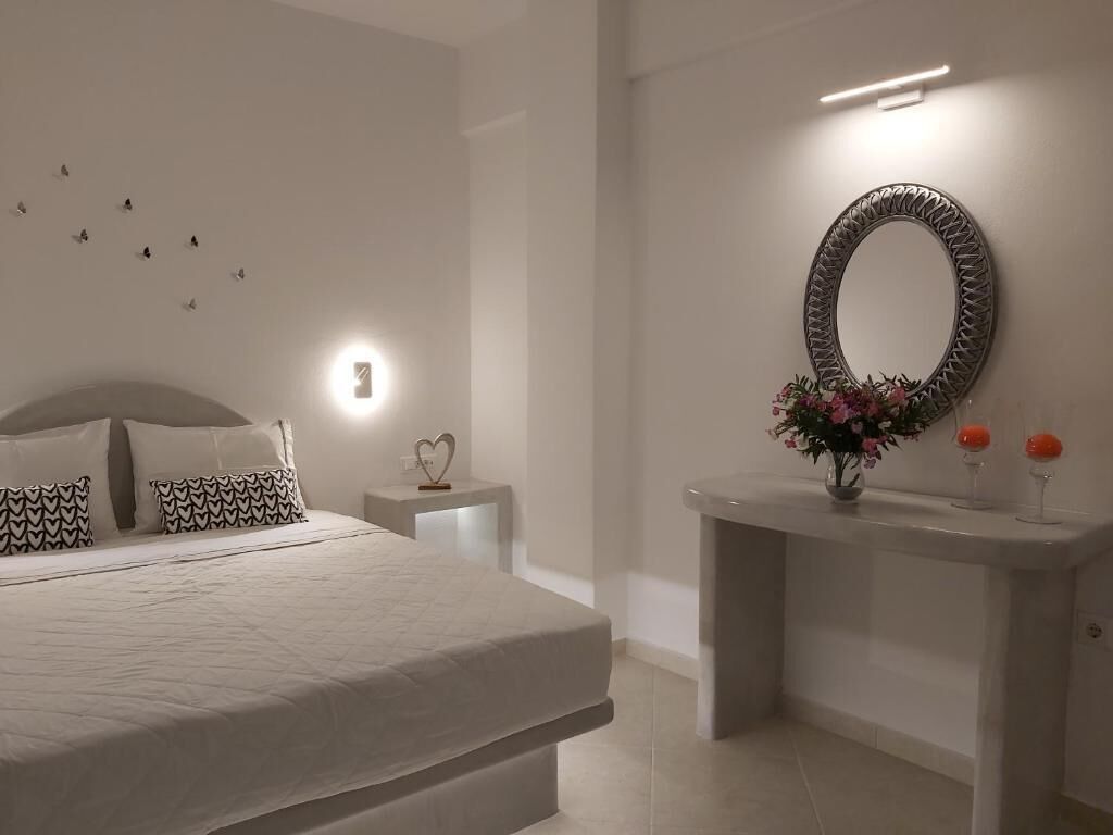 A modern bedroom with a large bed, bedside tables, a wall-mounted mirror, and a small vase with flowers.