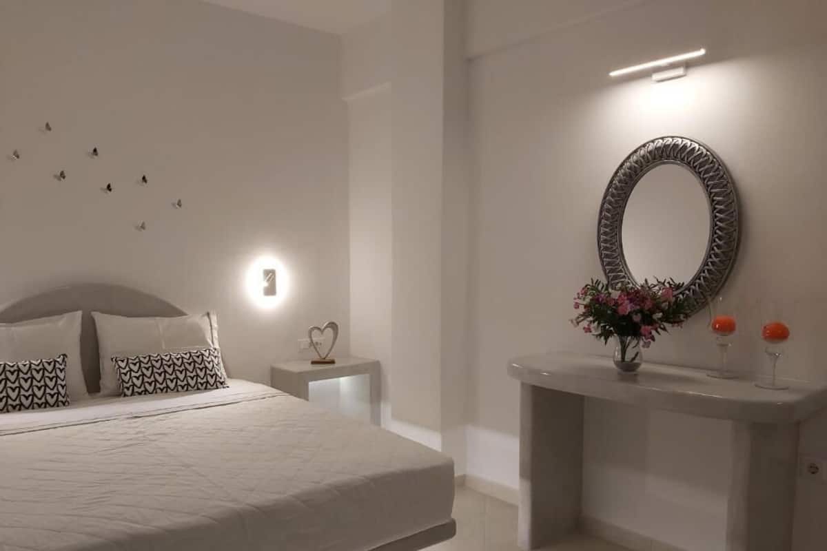 Un dormitorio moderno con una cama grande, mesitas de noche, un espejo montado en la pared y un pequeño jarrón con flores.