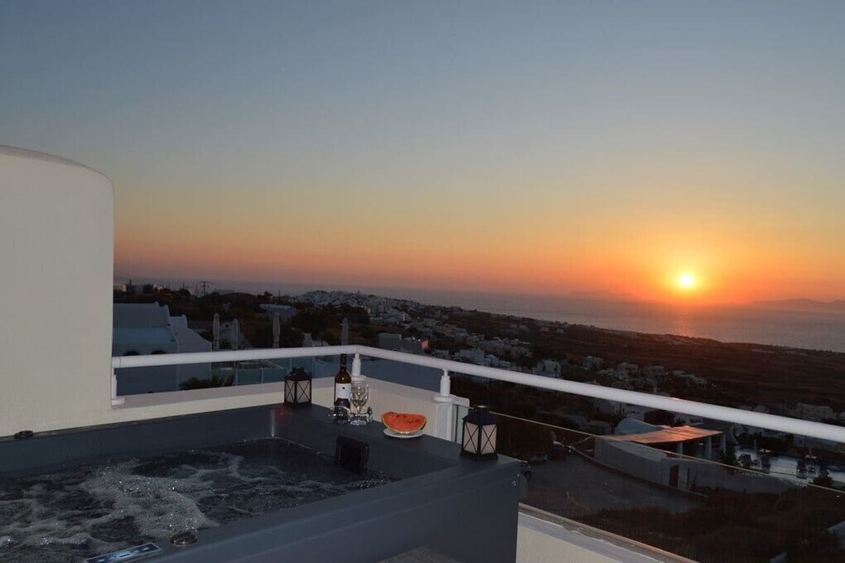Terraza en la azotea con vista al atardecer, bañera de hidromasaje y una mesa con una botella y un vaso.