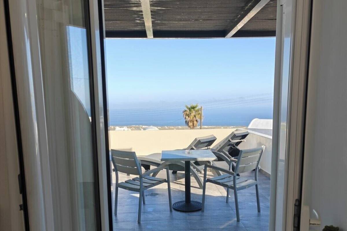 Una puerta de cristal da a un área de estar exterior con vista al mar.