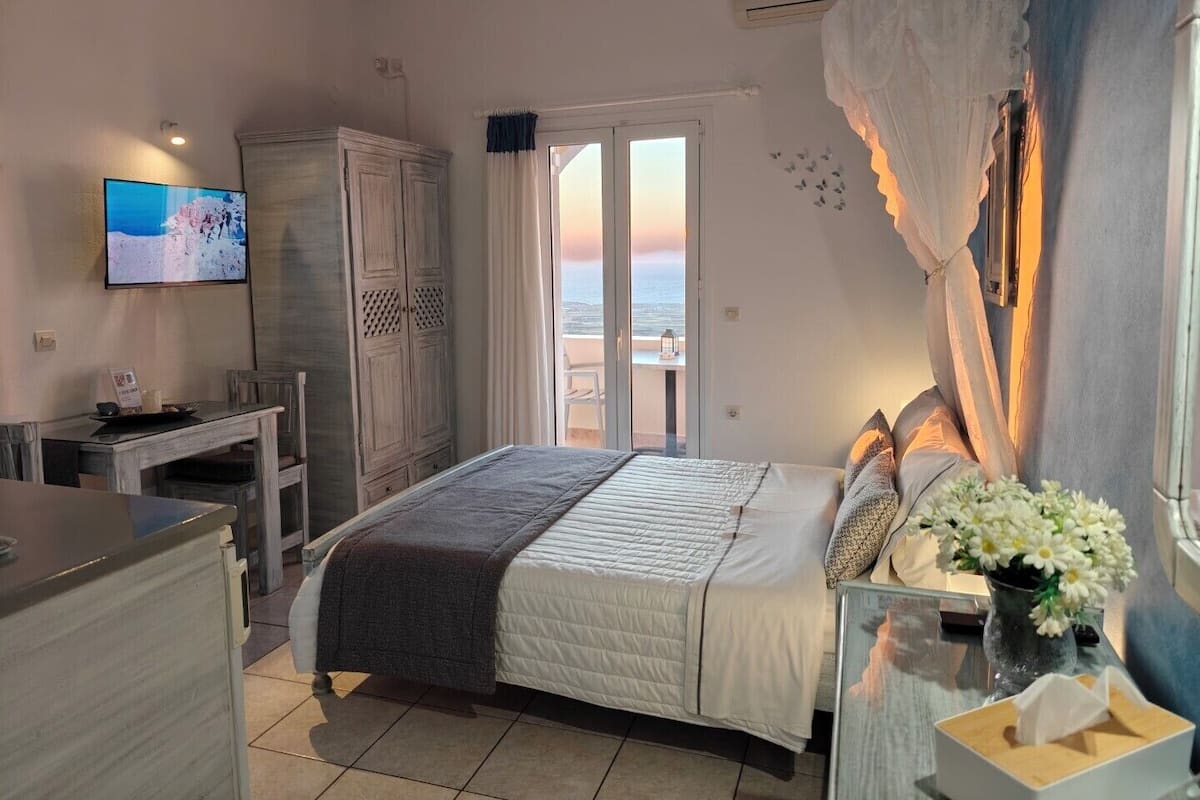 Un dormitorio con cama, televisión, armario, escritorio y vista al mar.