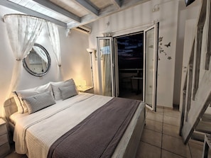 Un dormitorio con cama, mesitas de noche, un espejo y vistas al exterior.