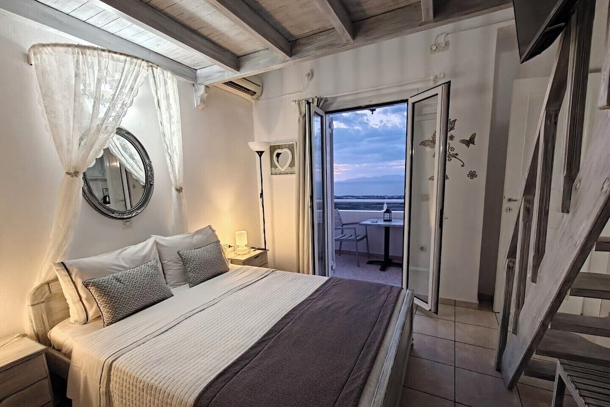 Un dormitorio con cama, mesita de noche y vista al mar a través de una puerta abierta.