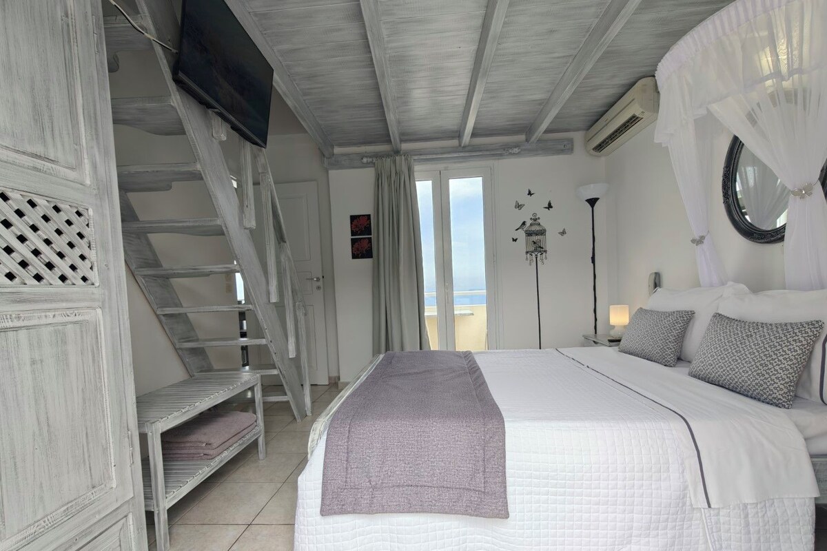 Un dormitorio con cama, televisión, escalera y vista al mar.