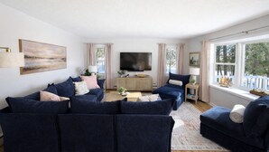 Una sala de estar con sofás azul oscuro, un televisor de pantalla plana y un ventanal con vistas a árboles.