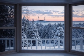 A view through a window with a white railing, featuring a snowy landscape and a bridge in the distance.
