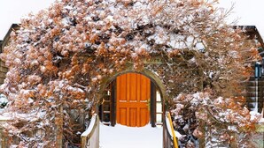 Un edificio cubierto de nieve con un arco de madera que conduce a una puerta roja.