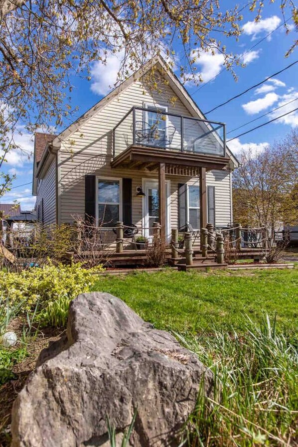 A two-story house with a balcony, a front porch, and a large rock in the foreground.