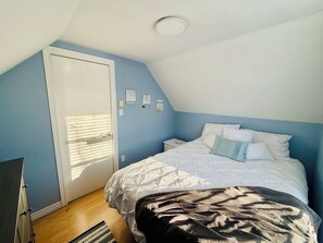 A bedroom with a bed, a nightstand, a door, and a window with blinds.
