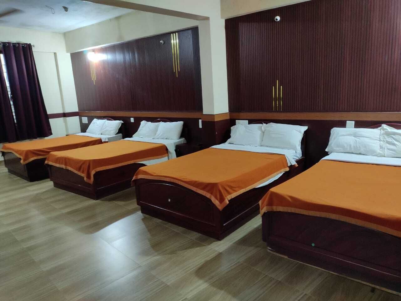 A hotel room with four beds, each with an orange bedspread and white pillows. The room has wooden headboards and a wooden floor.