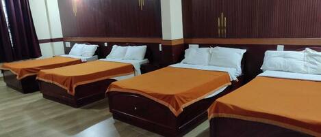 A hotel room with four beds, each with an orange bedspread and white pillows. The room has wooden headboards and a wooden floor.