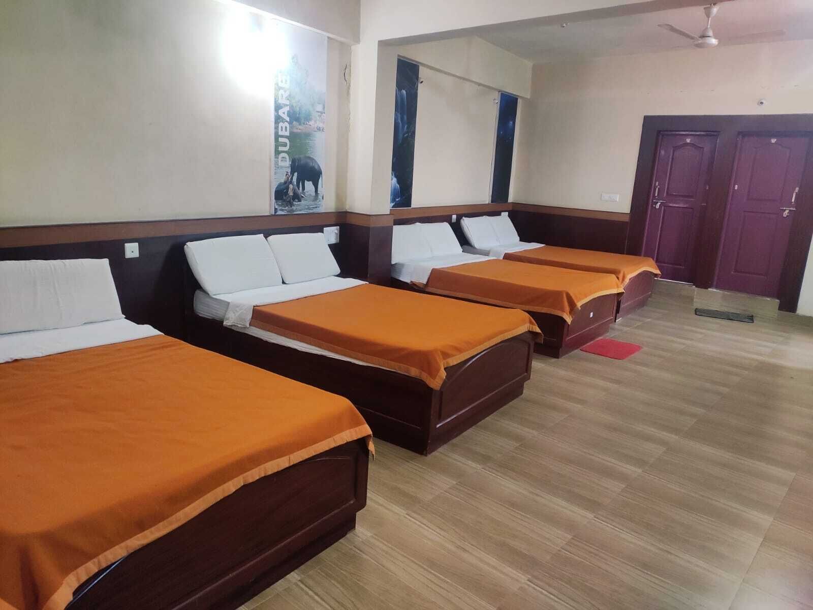 A hotel room with four single beds, wooden headboards, and a wooden floor.