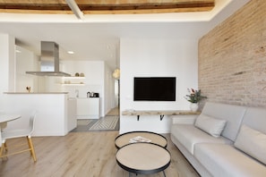 A modern living room with a sofa, two round tables, a TV mounted on the wall, and a kitchen in the background. - Comfort, style, and convenience all in one place!  ✨ - several units (Barcelona)