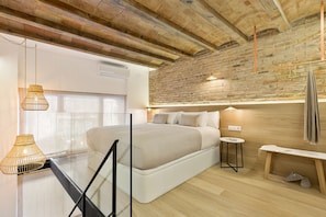 A modern bedroom with a large bed, a wooden headboard, and a brick wall. There are two pendant lights and a small bedside table with a lamp. - Comfort, style, and convenience all in one place!  ✨ - several units (Barcelona)