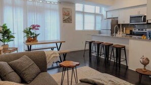 A modern kitchen with white cabinets, a microwave, and a stove. There is a dining area with a table and chairs, and a living room with a sofa and a coffee table. - Quiet charming townhome condo (Whitchurch-Stouffville)