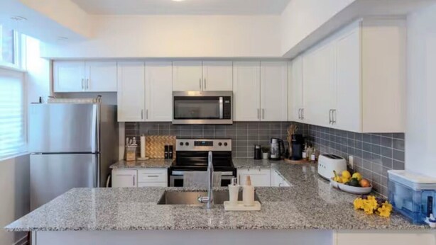 A modern kitchen with white cabinets, a stainless steel refrigerator, a microwave, an oven, and a granite countertop. - Quiet charming townhome condo (Whitchurch-Stouffville)