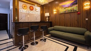 A hotel reception area with a marble wall, a chandelier, a sofa, and three bar stools. - CIEL ROSE HOTEL (Phu Quoc)
