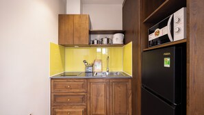 A compact kitchen with wooden cabinets, a black refrigerator, and a yellow backsplash. - CIEL ROSE HOTEL (Phu Quoc)