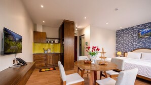 A hotel room with a bed, a dining table with chairs, a kitchen area, and a TV mounted on the wall. - CIEL ROSE HOTEL (Phu Quoc)