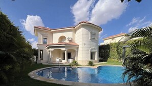 Une maison à deux étages avec une piscine, entourée de verdure.