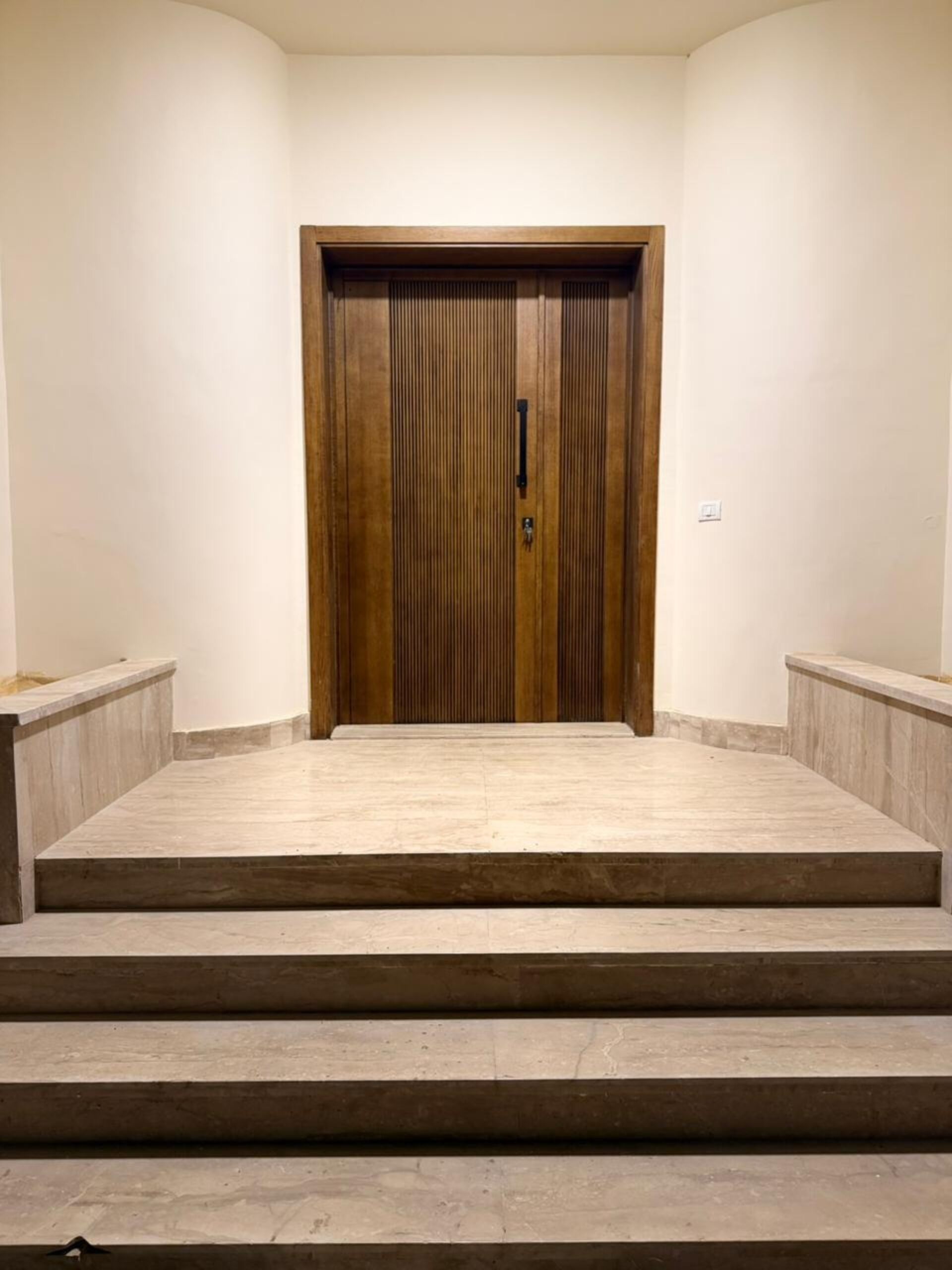 A wooden door with a keyhole and a handle, flanked by two small steps leading up to it.