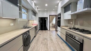 Une cuisine moderne dotée d’appareils électroménagers intégrés, d’un lave-linge et d’un coin repas visible à travers une porte ouverte.