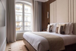 Ein Hotelzimmer mit einem großen Bett, Blick auf Gebäude durch ein Fenster, einem Heizkörper und einer Wandleuchte.