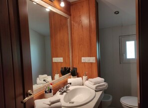 Ein Badezimmer mit einem Holzkosmetikschrank, einem großen Spiegel, einem Waschbecken und einer Toilette.
