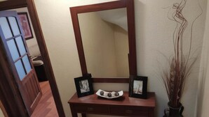 Uma toucador de madeira com espelho, duas fotografias emolduradas, um prato decorativo e um vaso com plantas secas.