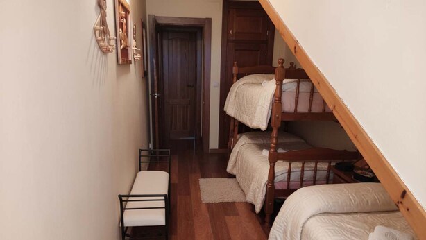 Um corredor estreito com uma cama de solteiro, uma cama beliche e um banco.