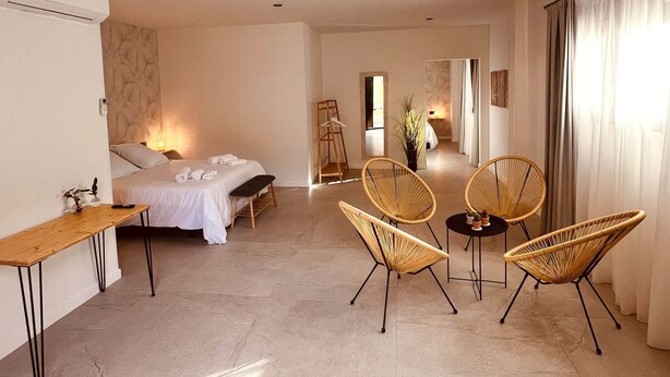 A spacious hotel room with a bed, a desk, and two wicker chairs. - Kirana Rural Apartment in Urdaibai (Bermeo)