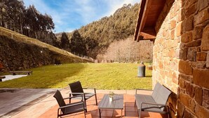 An outdoor patio with tiled flooring, a stone wall, and a view of a forested hillside. - Kirana Rural Apartment in Urdaibai (Bermeo)