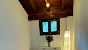 A dining area with a wooden table and chairs, a vase with flowers, a window with blinds, and a floor lamp. - Kirana Rural Apartment in Urdaibai (Bermeo)