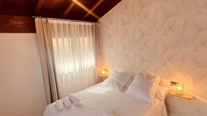 A neatly made bed with white linens and rolled towels, a wooden bench at the foot of the bed, and a textured wall behind the bed.