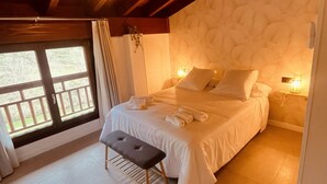 A bedroom with a large bed, a bench, a window, and a wooden ceiling.