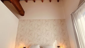 A bedroom with a wooden ceiling, a textured wall, a bed with white linens, and two bedside lamps.