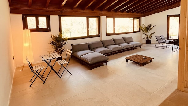 A spacious living area with a high wooden ceiling, a sectional sofa, a coffee table, and a dining area with chairs.