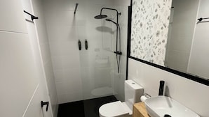 Un baño moderno con ducha acristalada, inodoro blanco y tocador de madera con lavamanos.
