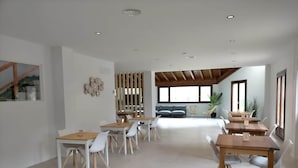Un comedor amplio y moderno con sillas blancas y mesas de madera, un ventanal con vistas y una estructura de techo de madera.