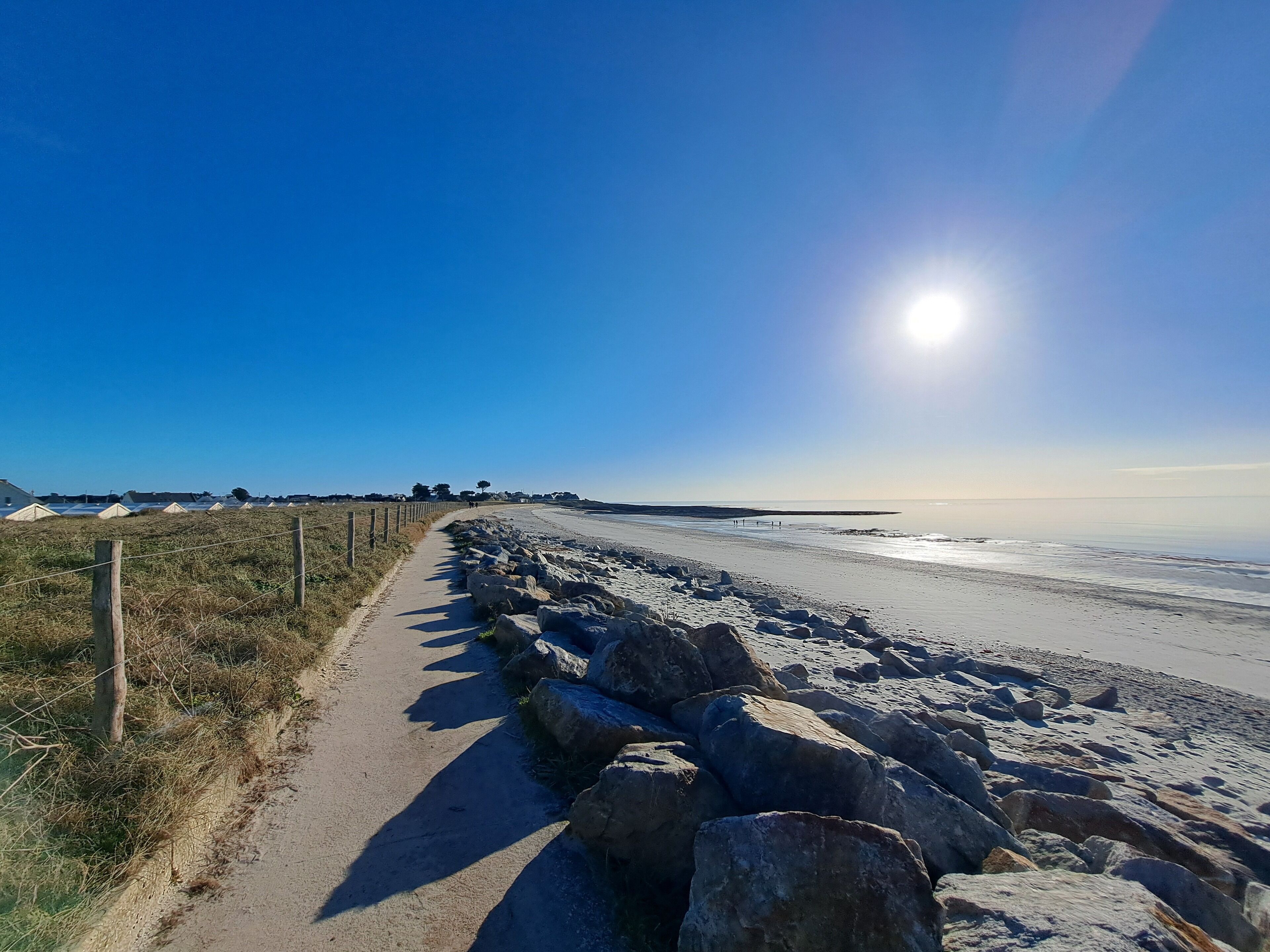 A beach with a paved walkway, large rocks, and a clear sky.