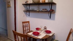 En matplats med ett träbord och stolar, en hylla ovanför bordet där tallrikar och glas står, och en mönstrad matta på golvet.