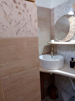 A bathroom with a round mirror, a white sink, and a wooden cabinet. - 25 m² of comfort, terrace, quiet location, 300 m from the lagoon and downtown (Sainte-Anne)
