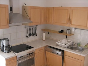 A compact kitchen with wooden cabinets, a built-in stove, a dishwasher, and a countertop with a coffee maker. - Finca Can Jan (Llucmajor)