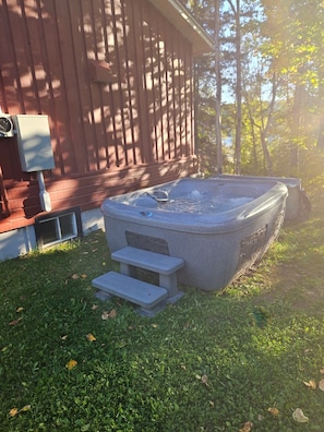 Un jacuzzi con escalones que lo rodean, situado sobre un césped frente a un edificio de madera.