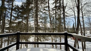 A snow-covered landscape with a wooden deck and a view of a forest.