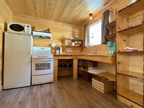 Una cocina funcional equipada con refrigerador, estufa, microondas y estantes de madera.